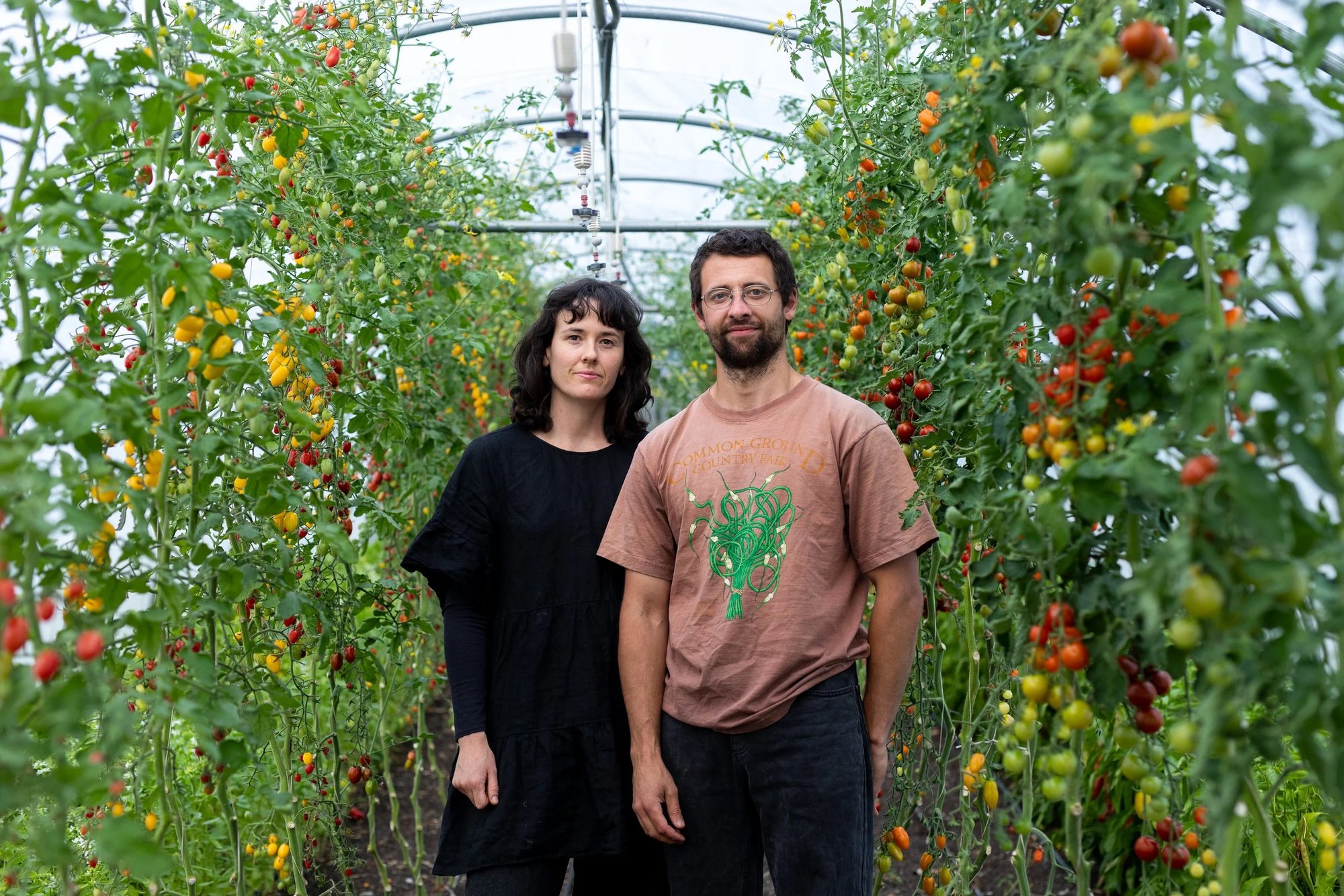Grace and Dylan standing together in a poly tunnel among tomato plants